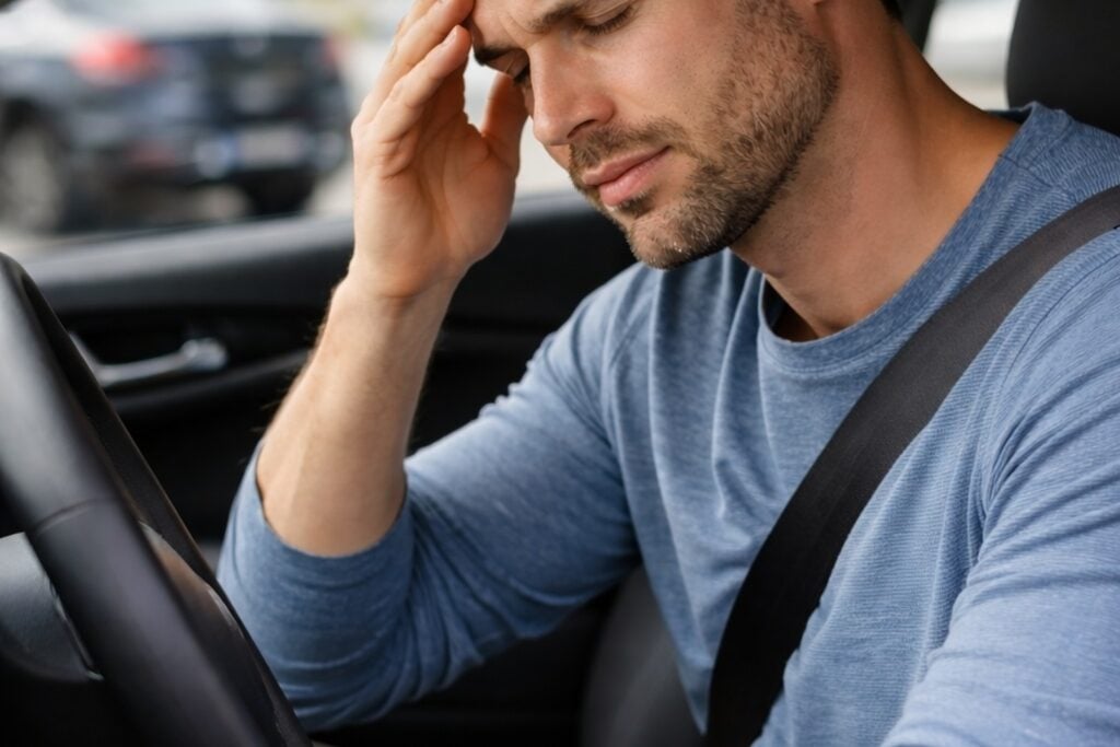 Overlooked vehicle symptoms shown by a driver rubbing his head inside a car shortly after a vehicle collision.