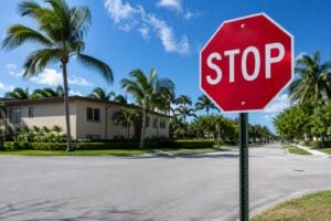Red stop sign on a quiet residential street corner in South Florida with palm trees and a stucco building in the background under bright midday sun