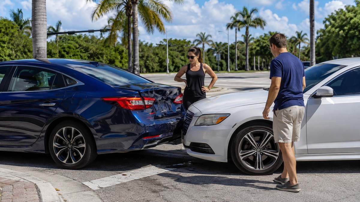 Two drivers assessing a minor rear-end collision at a sunny Florida intersection