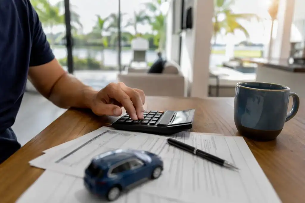 Person using a calculator over car insurance paperwork at a kitchen table